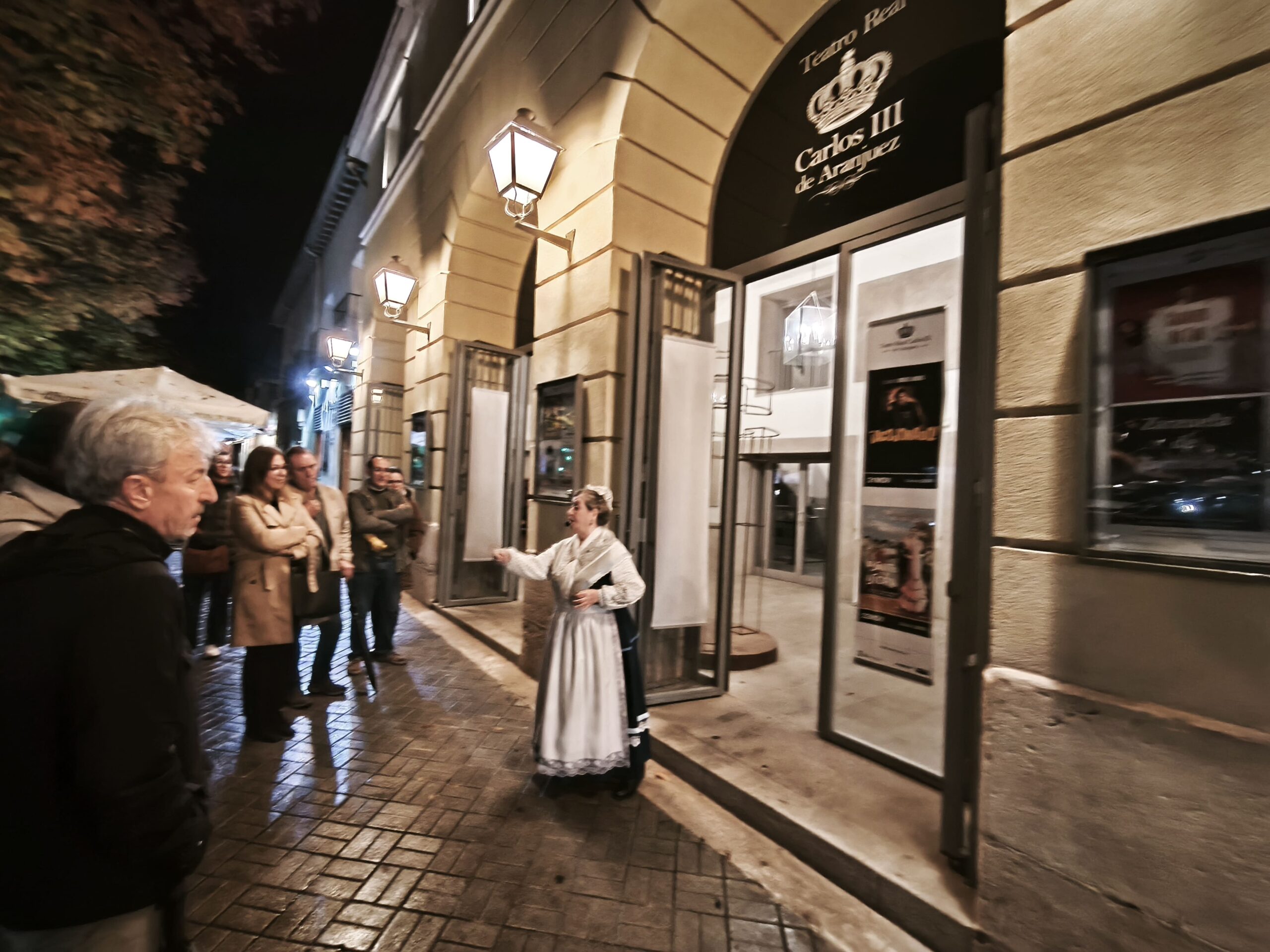 Grupo de visitantes ante la entrada iluminada del Teatro Real Carlos III de Aranjuez durante una visita nocturna